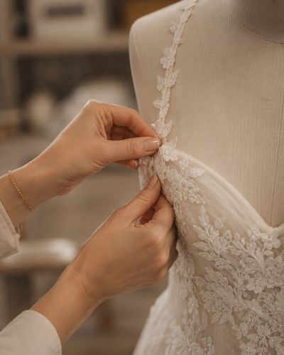 A lace shoulder strap pinned on an ivory bridal gown on a dressmaker's form